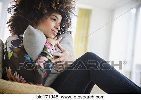 Stock Photo - Mixed race woman hugging pillow in armchair. Fotosearch
