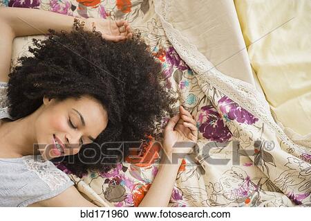 Stock Image - Mixed race woman laying on bed. Fotosearch