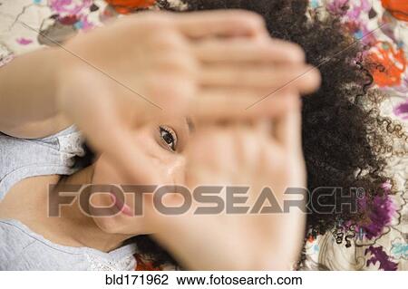 Mixed race woman peering through fingers on bed View Large Photo Image Stock Image - Mixed race woman peering through fingers on bed. Fotosearch