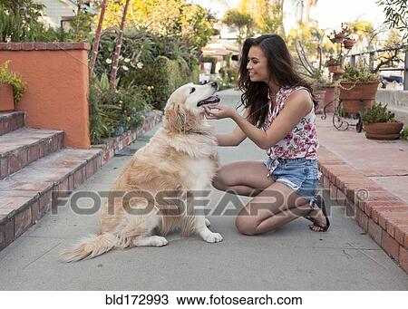Stock Image - Mixed race woman petting dog on sidewalk. Fotosearch
