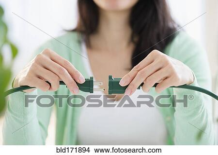 Picture - Mixed race woman plugging into extension cord. Fotosearch
