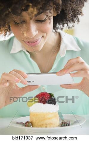Stock Photo - Mixed race woman taking cell phone photograph of dessert. Fotosearch