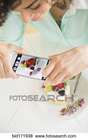 Stock Photo - Mixed race woman taking cell phone photograph of dessert. Fotosearch