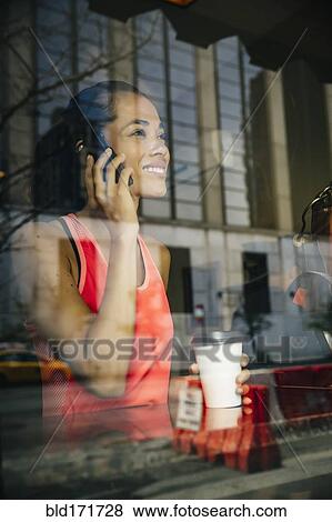 Stock Photo - Mixed race woman talking on cell phone in cafe. Fotosearch