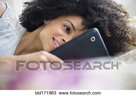 Stock Image - Mixed race woman using digital tablet on bed. Fotosearch