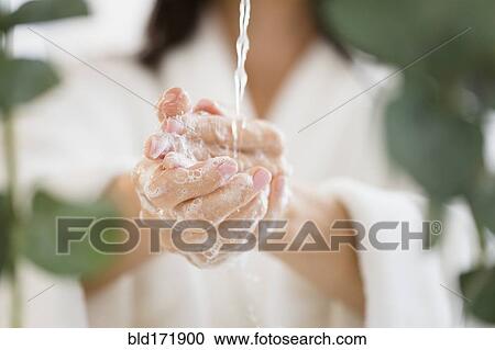 Stock Image - Mixed race woman washing her hands in water. Fotosearch