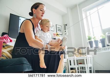 Stock Image - Mother helping son put on shoes in living room. Fotosearch