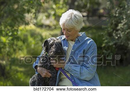 Picture - Older Caucasian woman hugging dog in park. Fotosearch