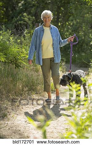 Stock Image - Older Caucasian woman walking dog on dirt path. Fotosearch