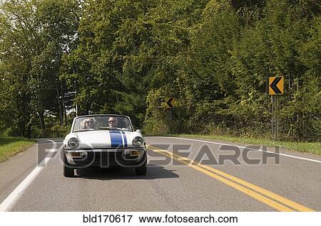 Stock Photo - Older couple driving convertible on rural road. Fotosearch