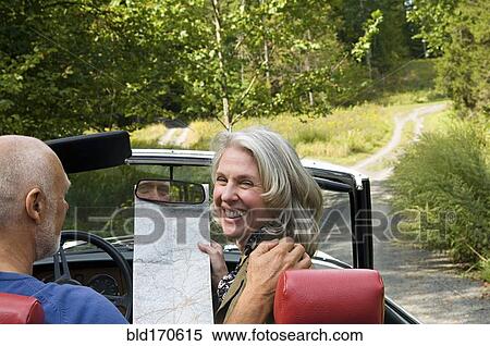 Stock Photography - Older couple driving convertible on dirt road. Fotosearch