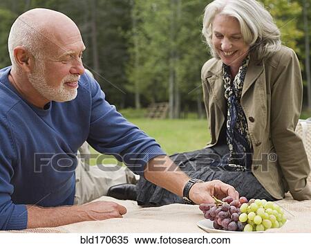 Stock Photography - Older couple eating grapes at picnic in park. Fotosearch