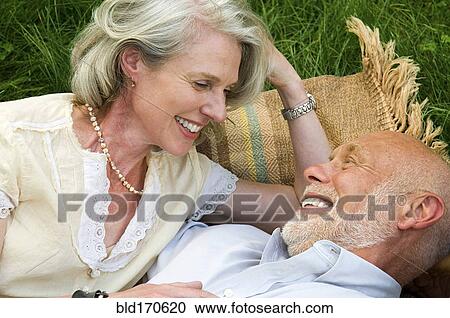 Stock Image - Older couple laying on picnic blanket. Fotosearch