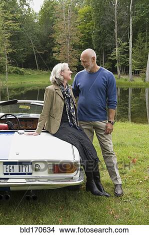 Picture - Older couple sitting on convertible in park. Fotosearch