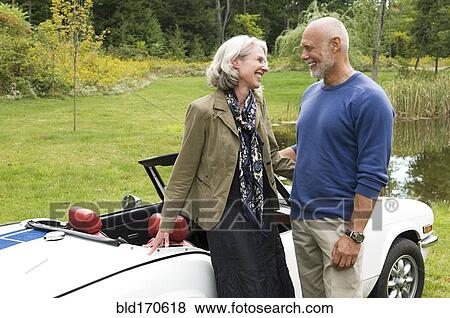 Stock Photo - Older couple standing by convertible. Fotosearch