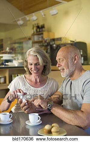 Stock Photograph - Older couple using cell phone in cafe. Fotosearch