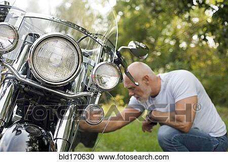 Older man repairing motorcycle in park View Large Photo Image Stock Image - Older man repairing motorcycle in park. Fotosearch