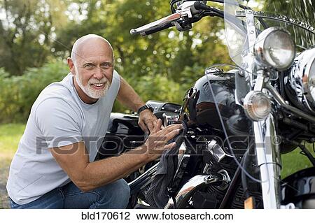 Stock Image - Older man repairing motorcycle. Fotosearch