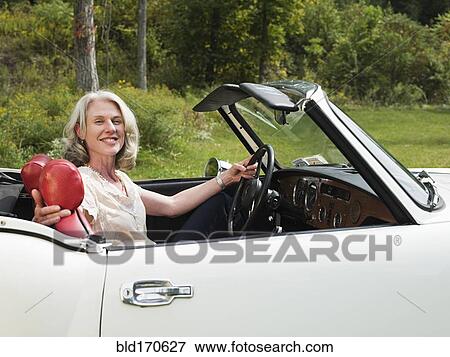 Stock Photo - Older woman driving convertible in park. Fotosearch
