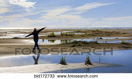 Stock Image - Older woman walking in marshy rural field. Fotosearch