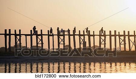 Stock Image - People walking on elevated wooden walkway at sunset. Fotosearch