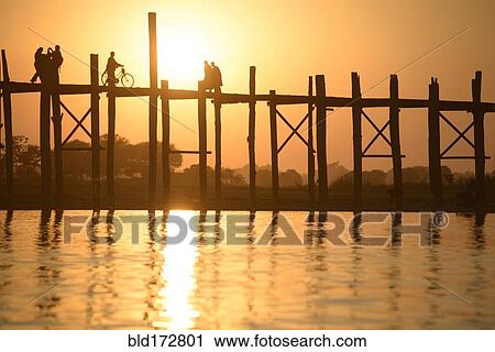 Stock Image - People walking on elevated wooden walkway at sunset. Fotosearch