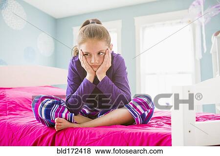 Stock Photo - Pouting Caucasian girl sitting on bed. Fotosearch
