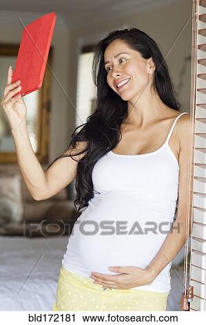 Stock Image - Pregnant Hispanic woman taking selfie with digital tablet. Fotosearch