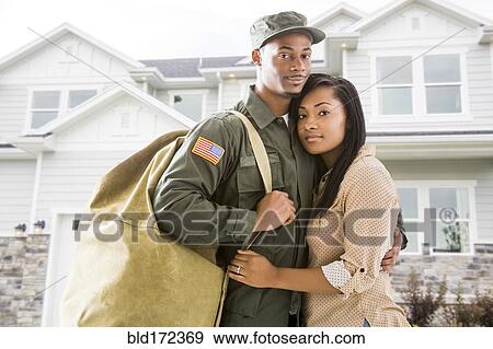 Stock Photo - Returning soldier and wife standing outside house. Fotosearch