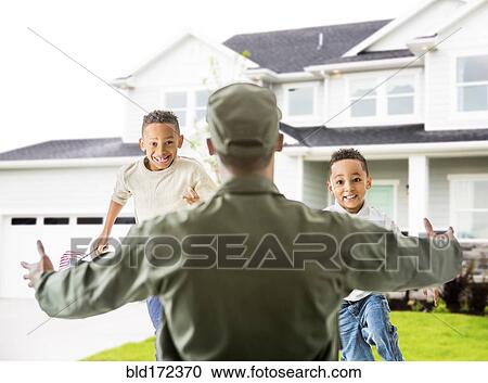 Stock Image - Returning soldier greeting children outside house. Fotosearch