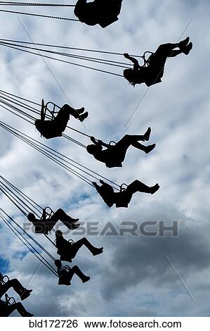 Stock Photograph - Silhouette of people riding chair swing under cloudy sky. Fotosearch