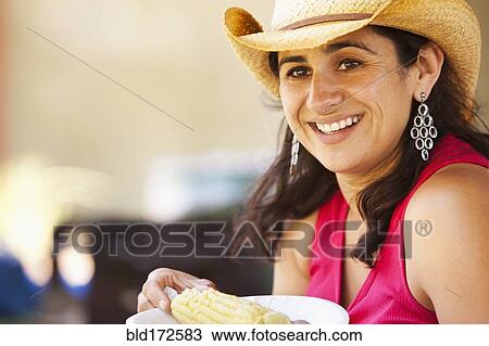 Stock Image - Smiling Hispanic woman eating corn. Fotosearch