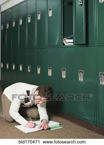 Stock Image - Student doing homework by locker in school hallway. Fotosearch