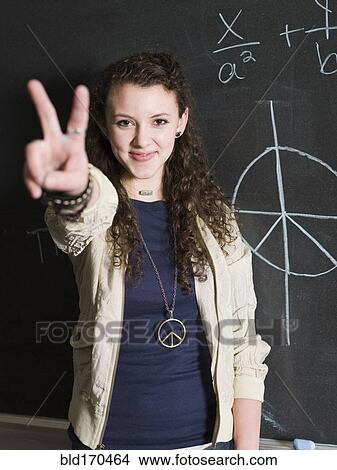 Picture - Student giving peace sign at chalkboard in classroom. Fotosearch