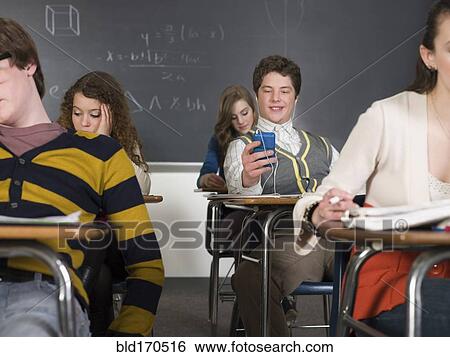 Stock Photograph - Student listening to earbuds at desk in classroom. Fotosearch