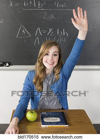 Stock Photography - Student raising her hand at desk in classroom. Fotosearch