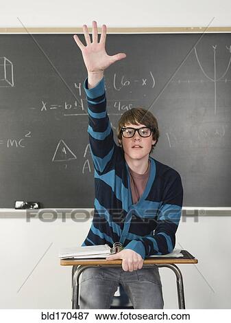 Stock Photo - Student raising his hand at desk in classroom. Fotosearch
