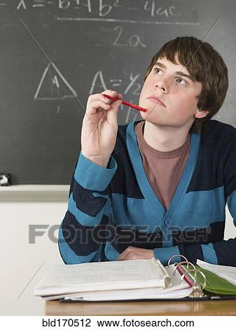 Stock Image - Student thinking at desk in classroom. Fotosearch
