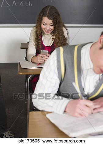 Stock Photography - Student using cell phone at desk in classroom. Fotosearch