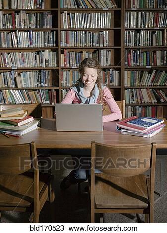 Stock Image - Student using laptop in library. Fotosearch
