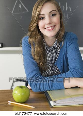 Stock Photo - Student with apple smiling at desk in classroom. Fotosearch