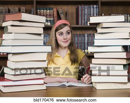 Stock Photograph - Student with stacks of books at desk in library. Fotosearch