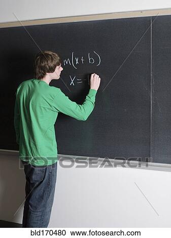 Stock Image - Student writing on chalkboard in classroom. Fotosearch