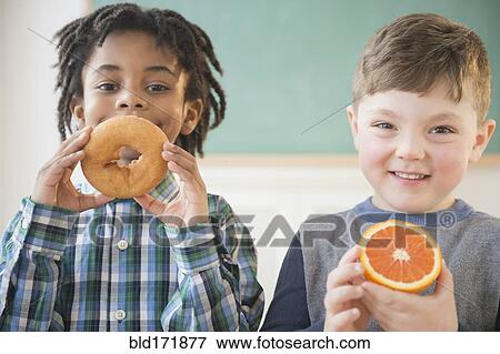 Stock Photo - Students eating donut and orange in classroom. Fotosearch