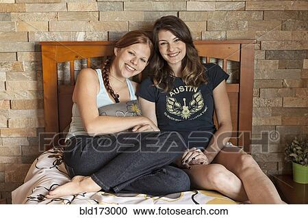 Stock Image - Students hugging on bed in dorm room. Fotosearch