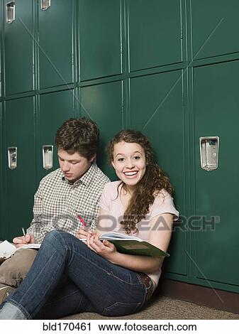 Stock Image - Students sitting at locker in school hallway. Fotosearch