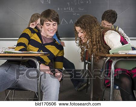 Stock Photograph - Students using cell phone at desk in classroom. Fotosearch