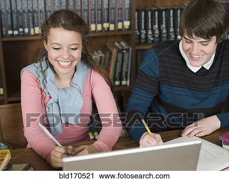 Stock Image - Students writing notes at desk in library. Fotosearch