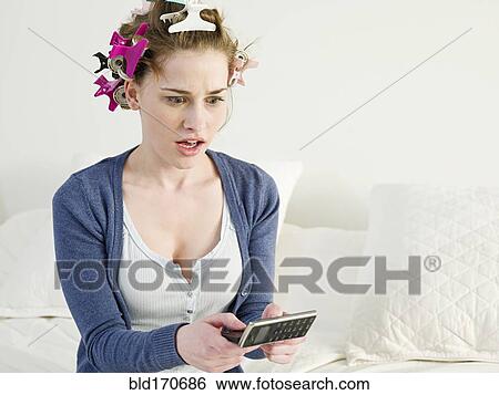 Stock Photograph - Surprised Caucasian woman using cell phone on sofa. Fotosearch
