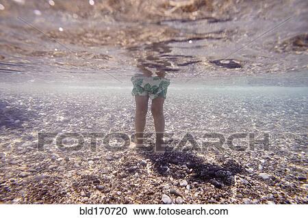Stock Image - Underwater view of Caucasian girl standing in ocean. Fotosearch
